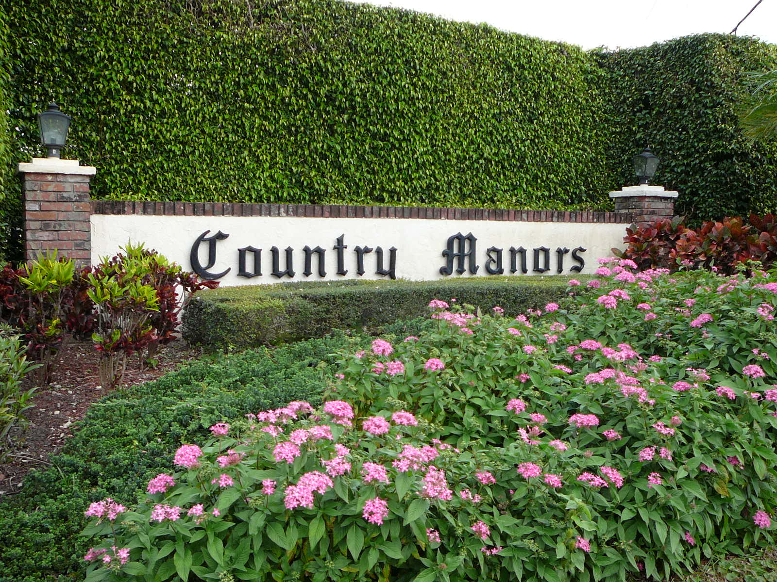 A sign that says country manors in front of some bushes